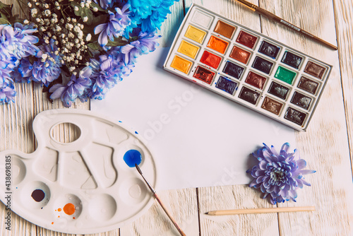 Palette of watercolor paints, brushes and paper for a water color on wooden background, close up. Flat lay, spring background with copy space