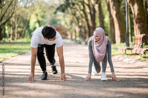 Young muslim couple in sport clothes standing in start position for run at green summer park. Man and woman in hijab preparing for morning workout outdoors.
