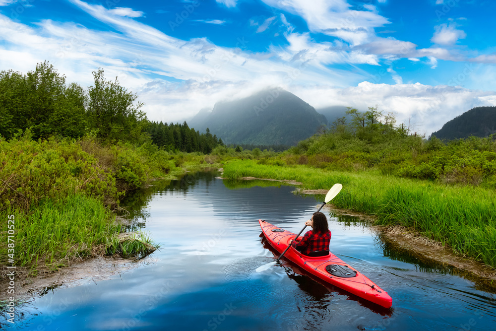 Adventure Caucasian Adult Woman Kayaking in Red Kayak surrounded by Canadian Mountain Landscape. Blue Sky Art Render. Widgeon Valley, Pitt Meadows, Vancouver, British Columbia, Canada. Adventure Caucasian Adult Woman Kayaking in Red Kayak surrounded by Canadian Mountain Landscape. Blue Sky Art Render. Widgeon Valley, Pitt Meadows, Vancouver, British Columbia, Canada.
