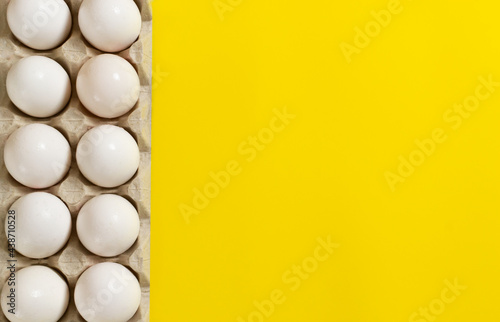 White chicken eggs lie in an egg tray on yellow background.