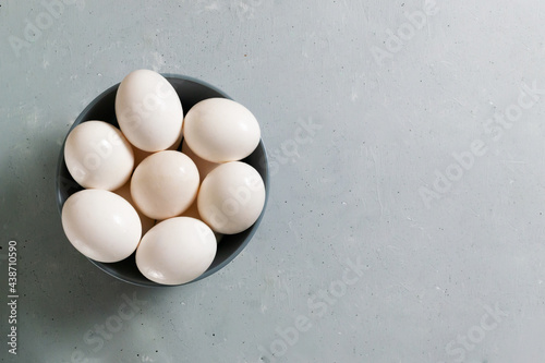 White chicken eggs lie in a gray bowl on a gray background.