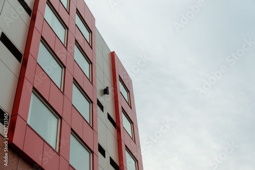 Commercial external metal composite panels on a building with blue sky and clouds in the background. The durable metal composite panels are both red and grey in color on the modern building.