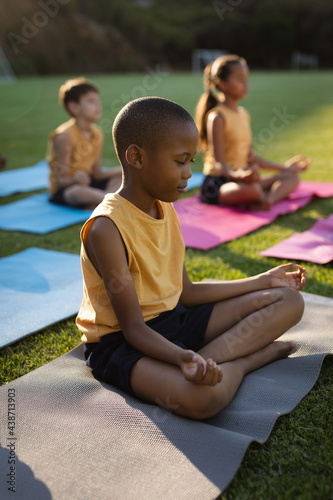 African american boy practicing yoga and meditating sitting on yoga mat in the garden at school