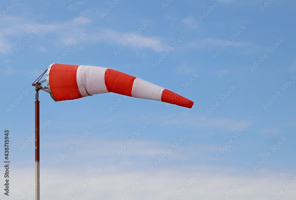 Red and white airport wind sock on blue sky with a few fluffy clouds blowing mostly straight out - obrazy, fototapety, plakaty 