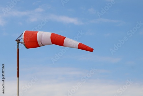 Red and white airport wind sock on blue sky with a few fluffy clouds blowing mostly straight out