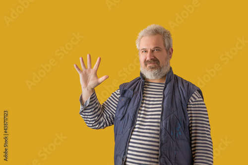 A man with a gray beard shows hand with fingers splayed. On a yellow isolated background.