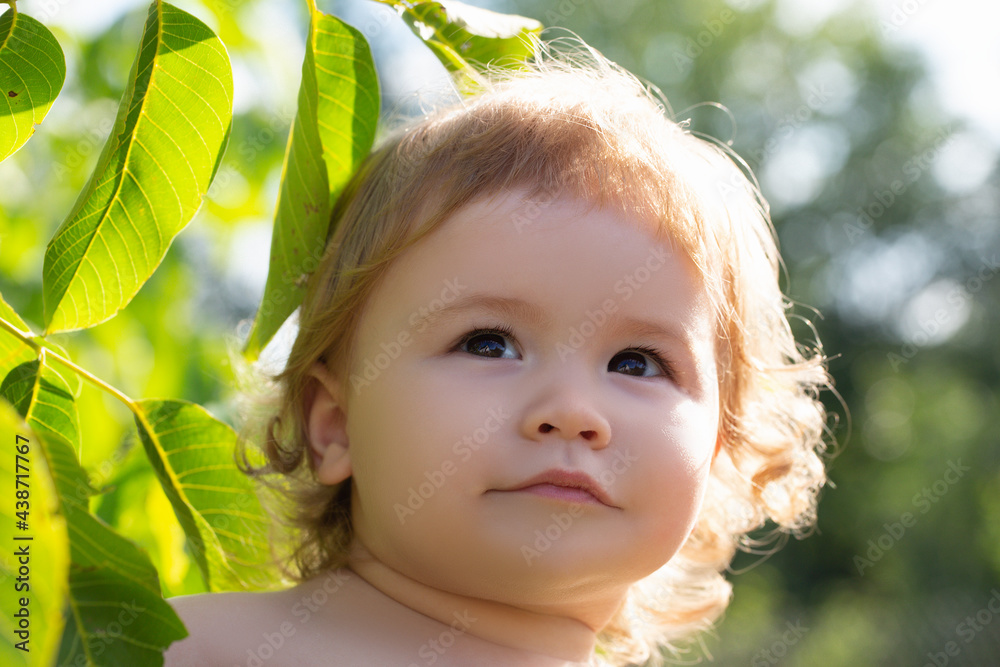 Caucasian child with green leaves portrait close up. Kids baby face in nature park. Caucasian child with green leaves portrait close up. Kids baby face in nature park.