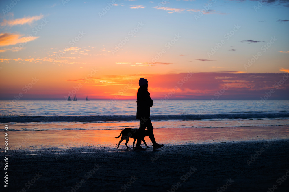 Woman walking with the dog on the beach. Beautiful sunrise, sun, blue sky with cloud and the sea landscape.