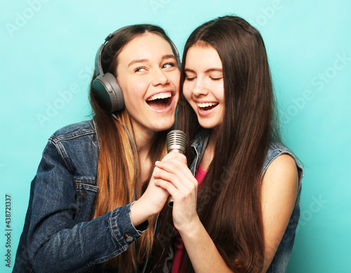 lifestyle, emotion and people concept: Two young girl friends standing together and listening to music and singing