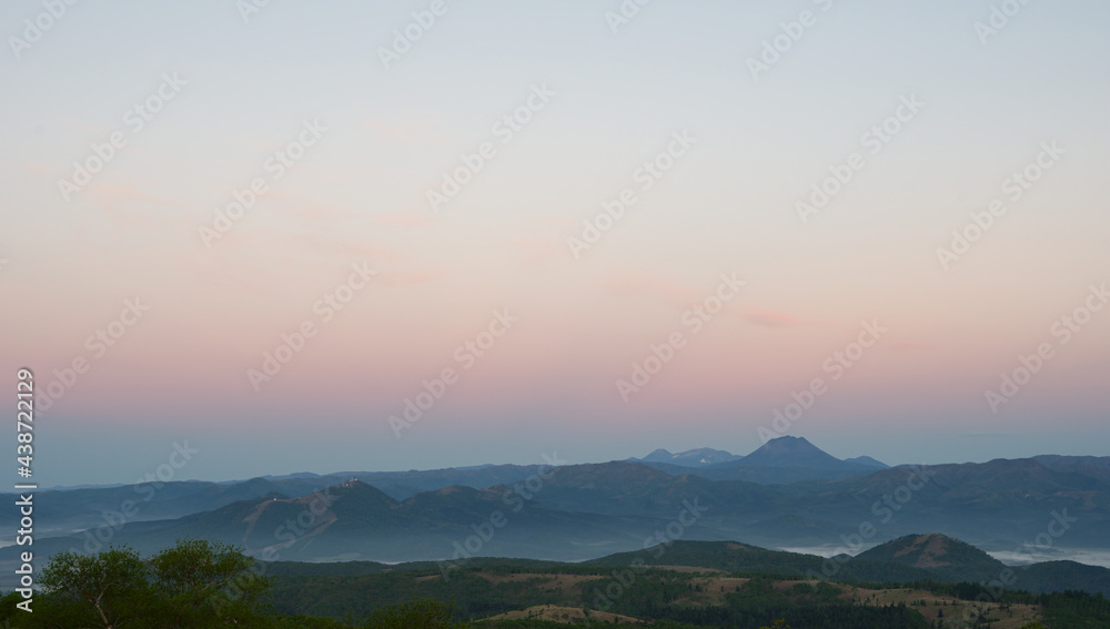 淡い色彩の夜明けの空と遠くの山のシルエット。