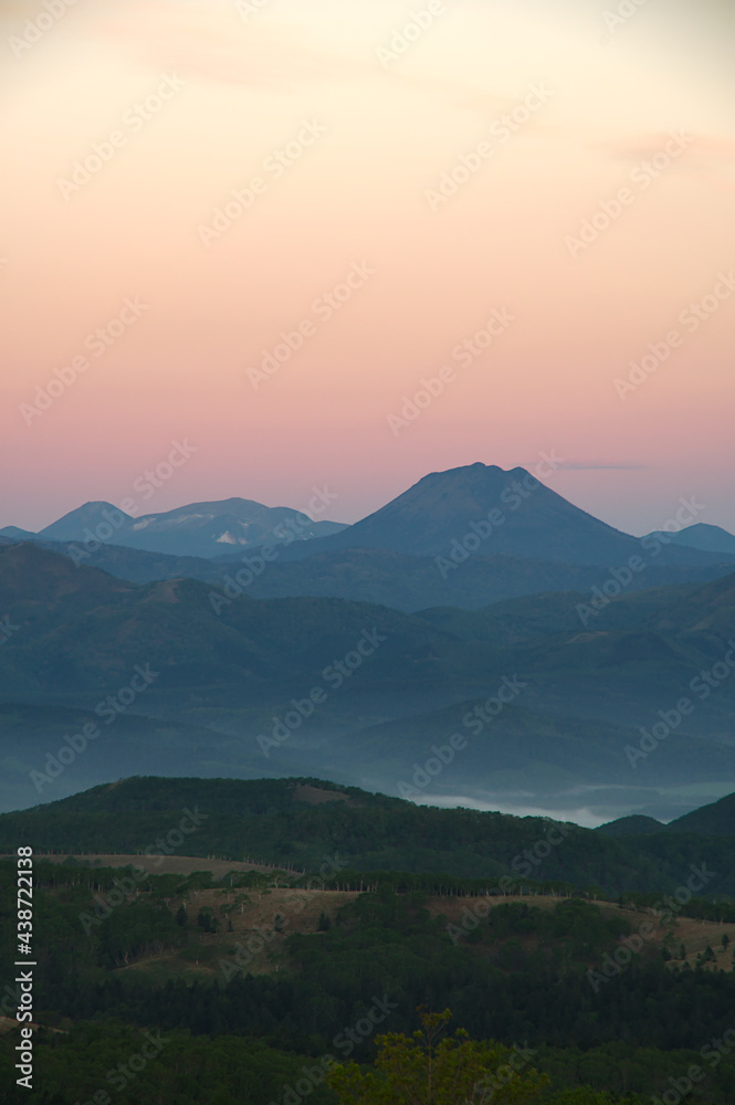 淡い色彩の夜明けの空と遠くの山のシルエット。