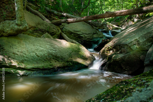 A small stream cascades down through some large rocks and into a pool of water in the middle of a forest in Hamilton, Ontario.