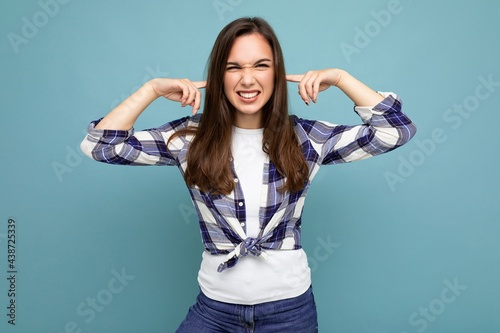 Don't want to hear it. Young emotional positive attractive brunette female person isolated on blue background with copy space and covering ears