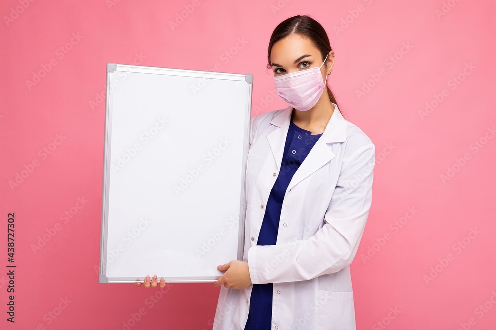 Woman doctor wearing a white medical coat and a mask holding blank board with copy space for text isolated on background. Coronavirus concept Woman doctor wearing a white medical coat and a mask holding blank board with copy space for text isolated on background. Coronavirus concept