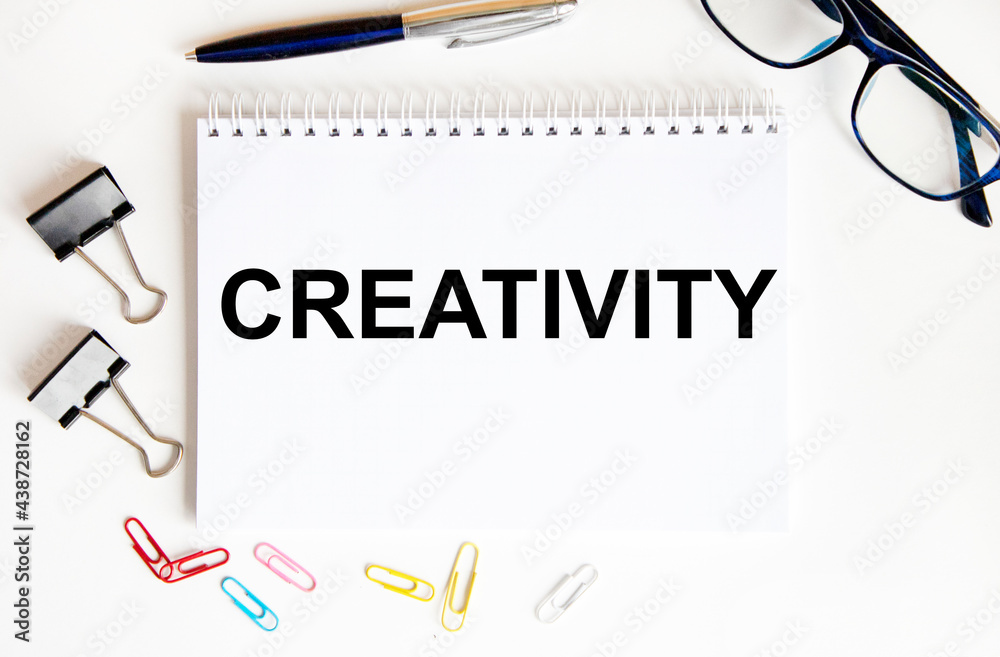 In the notebook is the text of Creativity, next to paper clips and clips for paper, glasses and pen. In the notebook is the text of Creativity, next to paper clips and clips for paper, glasses and pen.
