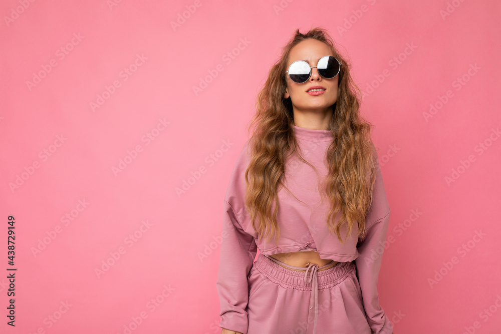 Photo shot of beautiful young dark blonde woman wearing casual clothes and stylish sunglasses isolated over colorful background looking at camera Photo shot of beautiful young dark blonde woman wearing casual clothes and stylish sunglasses isolated over colorful background looking at camera