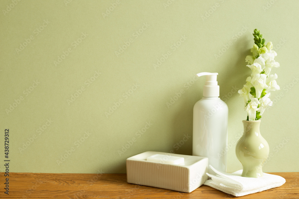 Shampoo bottle, soap, shower towel, flower on wooden table. khaki green wall background. Bathroom interior. Skin care and spa concept