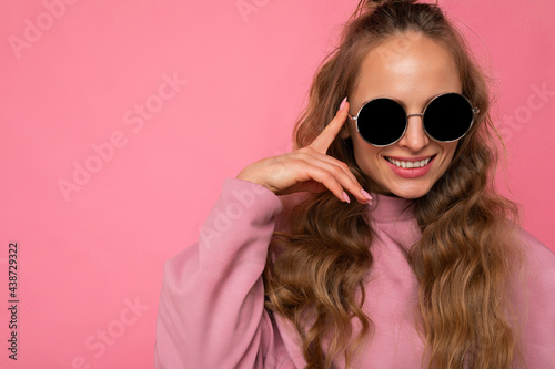 Closeup photo of pretty positive smiling young blonde curly woman isolated over pink background wall wearing casual pink sport clothes and stylish sunglasses looking at camera © Ivan Traimak