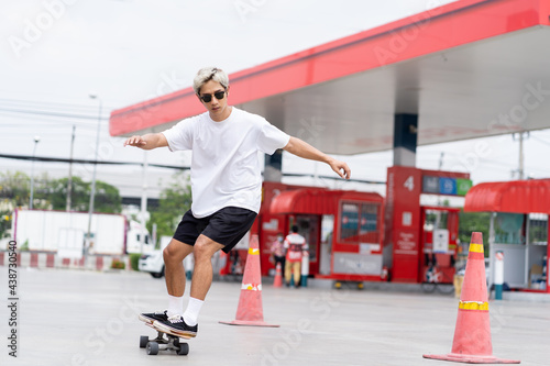 Asian young man skater riding on skateboard on courtyard at gas station with wear sunglasses. Young man teenager skateboarding outdoor