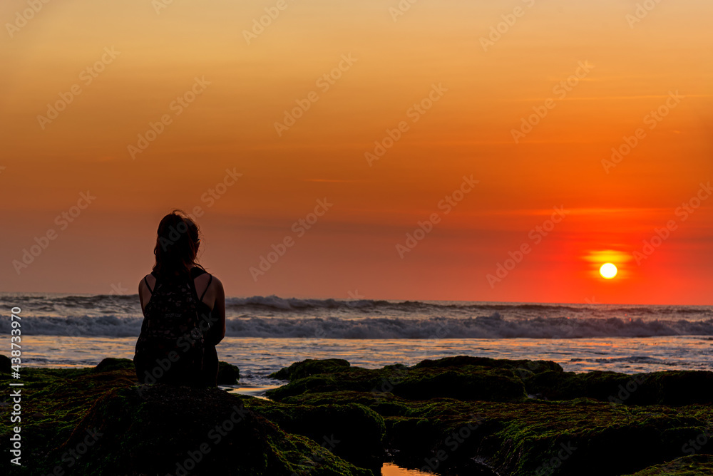 Silhouette of tourist sitting on a rock looking view the sunset over the sea in Bali, Indonesia.