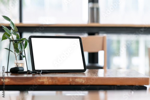 Blank screen tablet on wooden table in co-workspace with copy space.