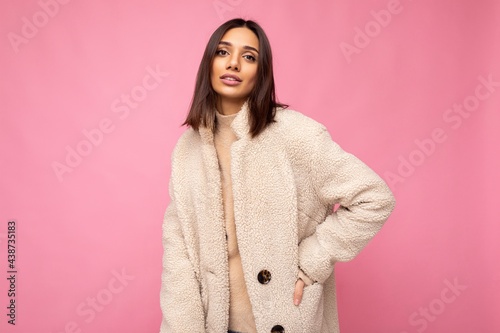 Caucasian photo of attractive self-confident stylish young brunette woman wearing autumn beaige warm coat isolated on pink background with empty space. Fashion concept photo