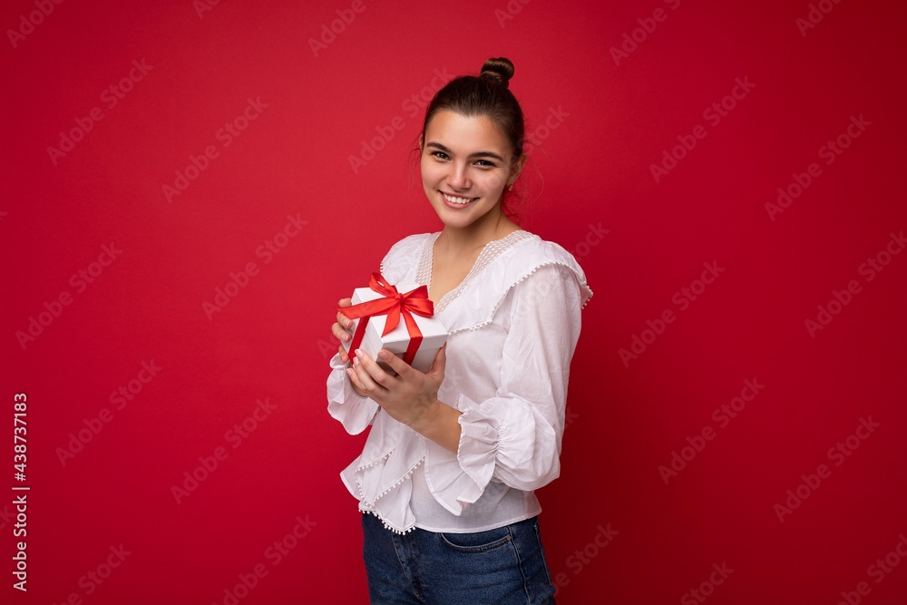 Shot of attractive positive smiling young brunette woman isolated over colourful background wall wearing everyday trendy outfit holding gift box and looking at camera Shot of attractive positive smiling young brunette woman isolated over colourful background wall wearing everyday trendy outfit holding gift box and looking at camera