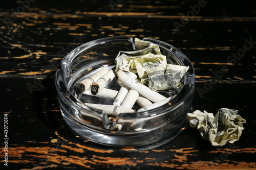 Fototapeta Naklejka Na Ścianę i Meble -  Ash tray with cigarettes and crumpled banknotes on dark wooden background