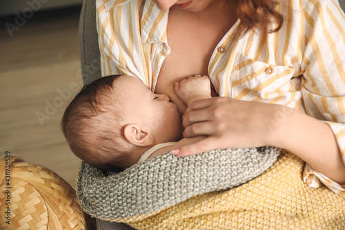 Young woman breastfeeding her baby at home, closeup photo