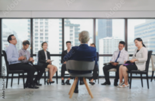 Soft blurred business background of senior caucasian male manager leading meeting with small asian team staff at city building office space.