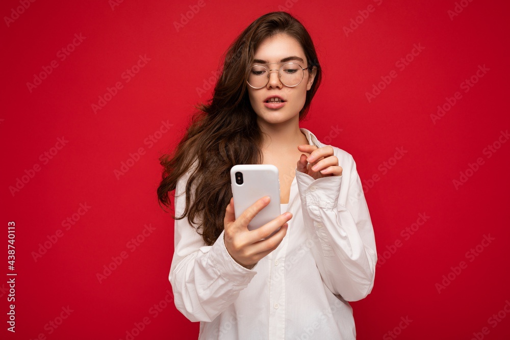 Beautiful young woman wearing casual clothes standing isolated over background surfing on the internet via phone looking at mobile screen Beautiful young woman wearing casual clothes standing isolated over background surfing on the internet via phone looking at mobile screen