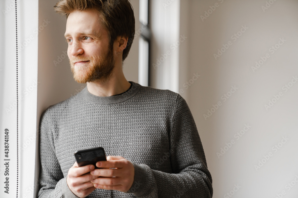 Ginger young man using mobile phone while leaning on wall indoors Ginger young man using mobile phone while leaning on wall indoors