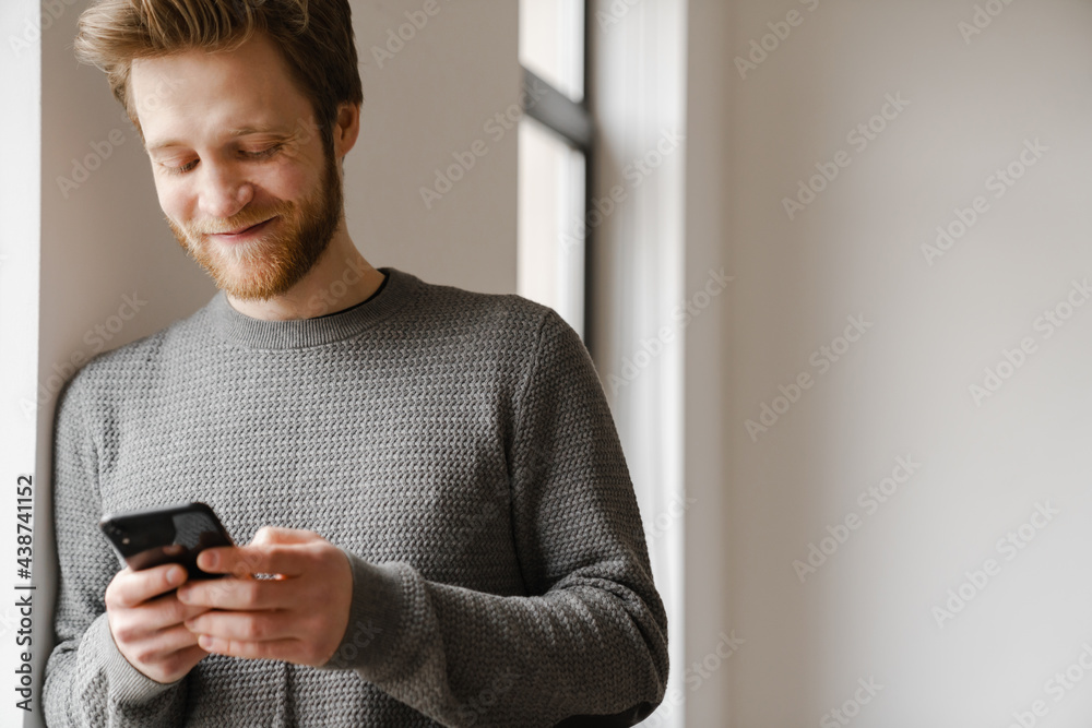 Ginger young man using mobile phone while leaning on wall indoors Ginger young man using mobile phone while leaning on wall indoors