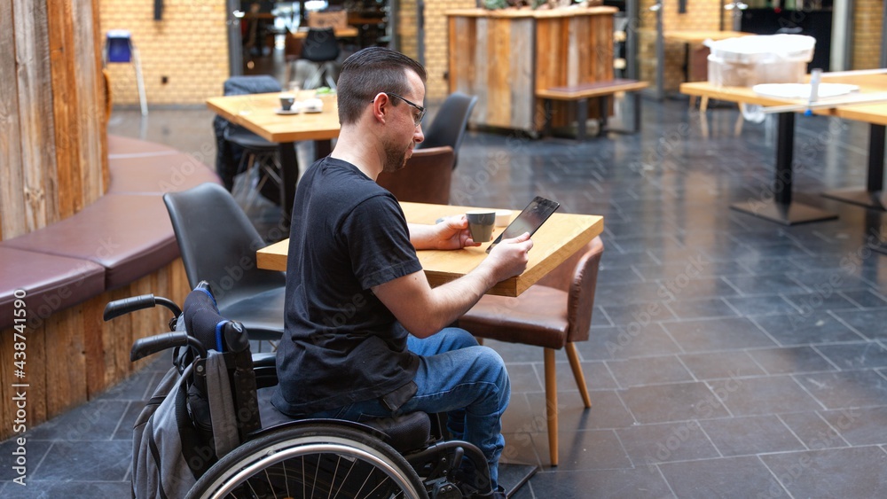 man in wheelchair looking at ipad tablet in restaurant man in wheelchair looking at ipad tablet in restaurant