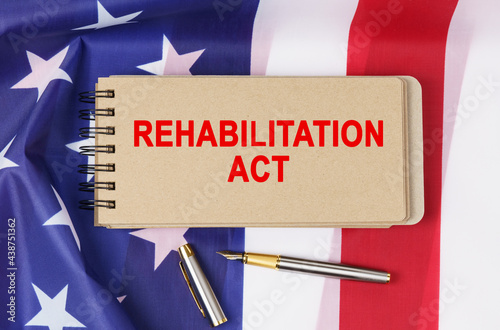 Against the background of the flag of the USA lies a notebook with the inscription - REHABILITATION ACT photo