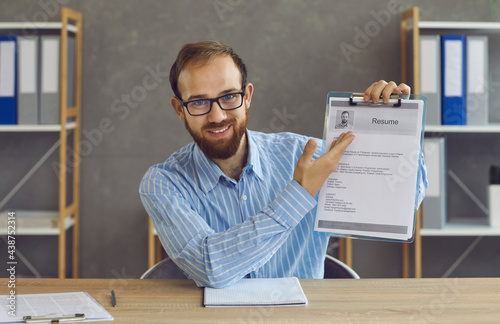 Unemployed jobless man holding printed CV on clipboard. Experienced work adviser shows resume sample form, gives job search tips, tells what information to include and how to sell skills and expertise