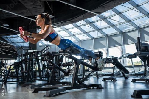 Young woman doing hyperextension with weighting at gym