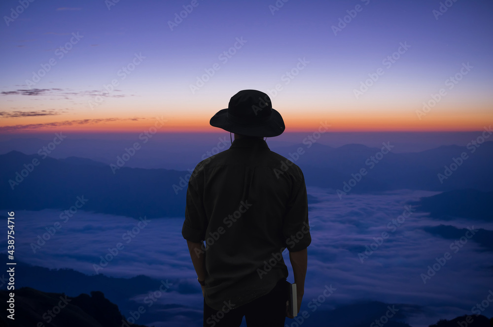 Silhouette of young traveler wearing black shirt and hat standing alone on top of the mountain and watched beautiful view of foggy landscape. It is a beautiful natural phenomenon in the morning.
