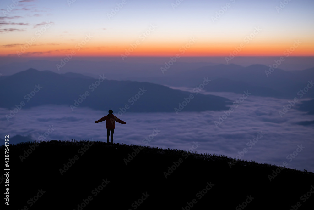 Silhouette of young traveler standing alone on top of the mountain and watched beautiful view of foggy landscape and sunrise in national park. It is a beautiful natural phenomenon in the morning.