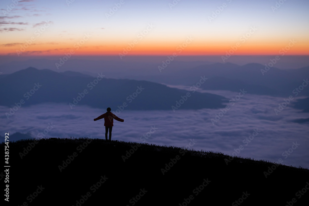 Silhouette of young traveler standing alone on top of the mountain and watched beautiful view of foggy landscape and sunrise in national park. It is a beautiful natural phenomenon in the morning. Silhouette of young traveler standing alone on top of the mountain and watched beautiful view of foggy landscape and sunrise in national park. It is a beautiful natural phenomenon in the morning.