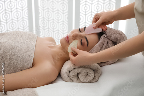 Young woman receiving facial massage with gua sha tools in beauty salon photo