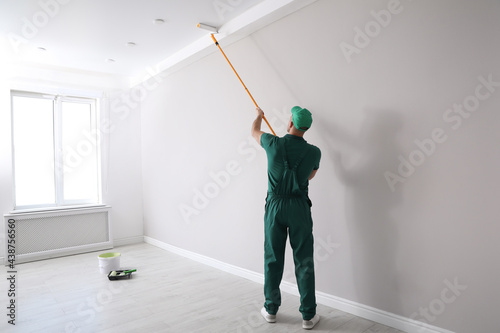 Fototapeta Naklejka Na Ścianę i Meble -  Man painting ceiling with roller in room, back view