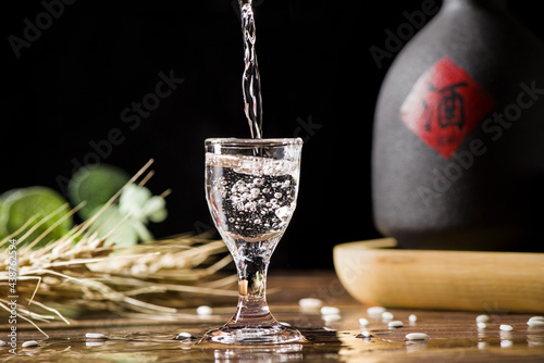 chinese liquor is poured into a glass from a bottle on wood background photo