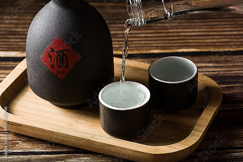chinese liquor is poured into a ceramic cup on wood background photo