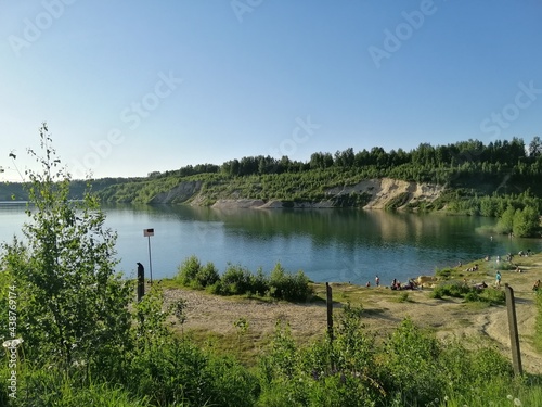 lake in an artificial quarry with sand hills, forests and people swimming in the water on the beach