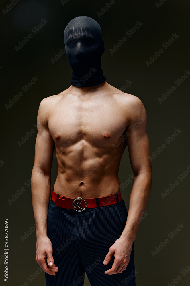 Fototapeta premium naked man with a pumped-up torso in trousers and with a mask on his head on a dark background