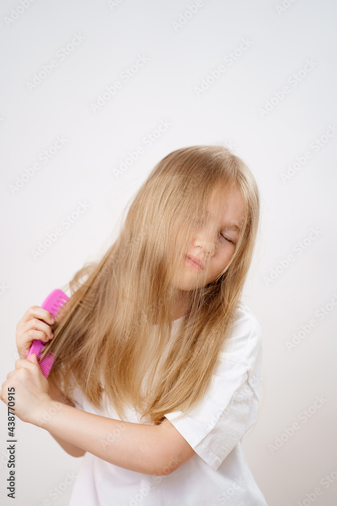 Fototapeta premium little girl combs long and tangled hair. white background.
