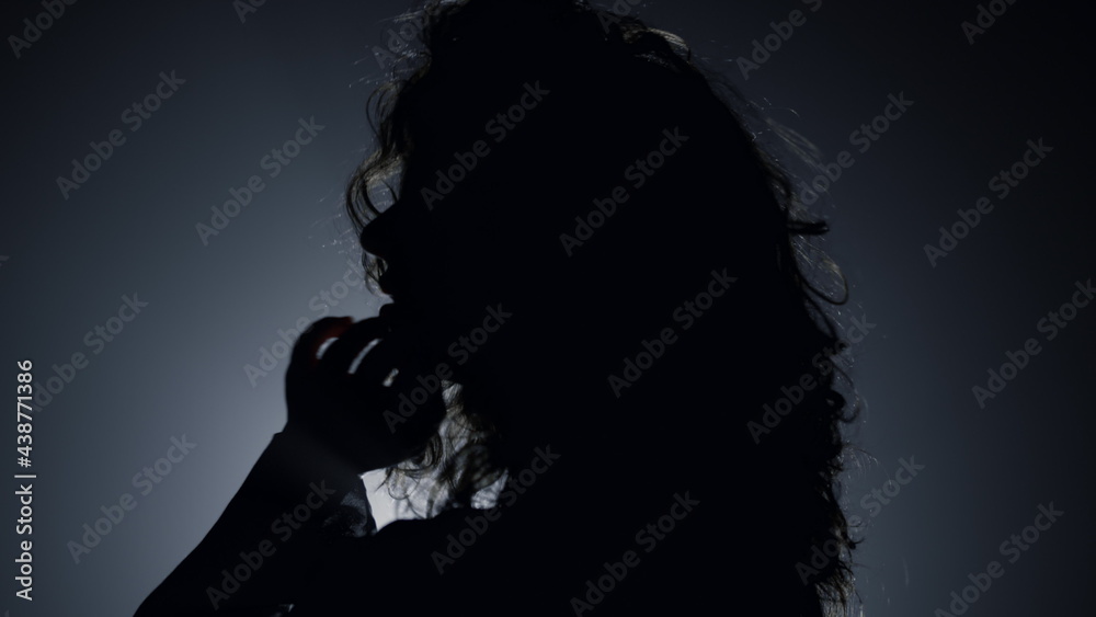 Silhouette pretty woman posing camera in dark. Passionate woman touching hair 