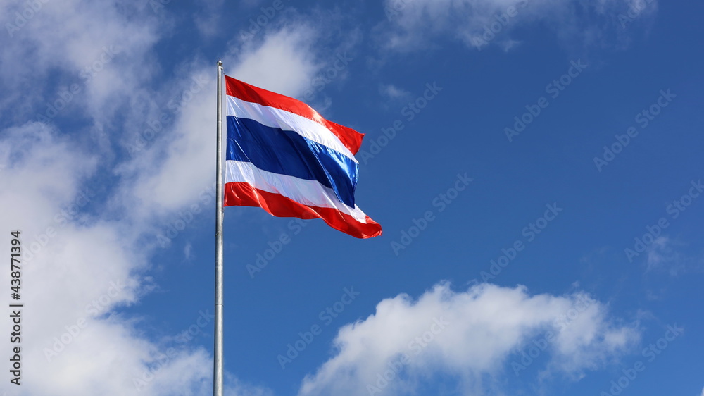 Thailand flag is fluttering in wind. Symbol of Thai nationality waving beautifully against blue sky background with white clouds.