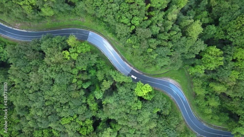 Aerial: white electric car driving on forest mountain road, twisty road corners photo
